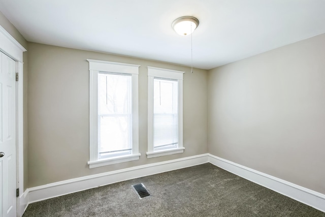 empty room featuring a wealth of natural light and dark carpet