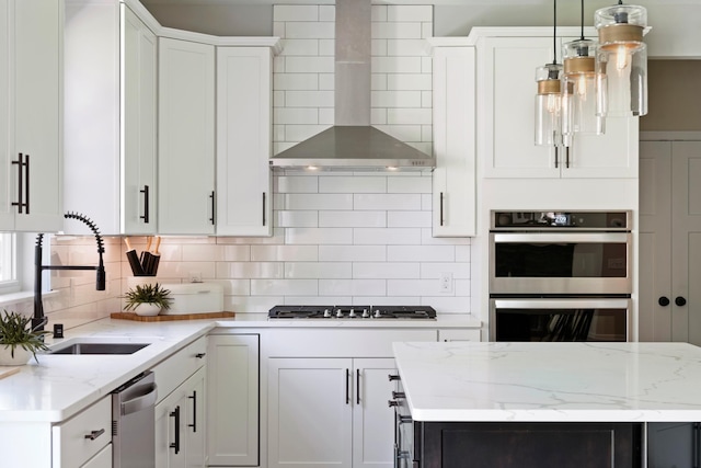 kitchen featuring decorative light fixtures, white cabinetry, sink, stainless steel appliances, and wall chimney range hood