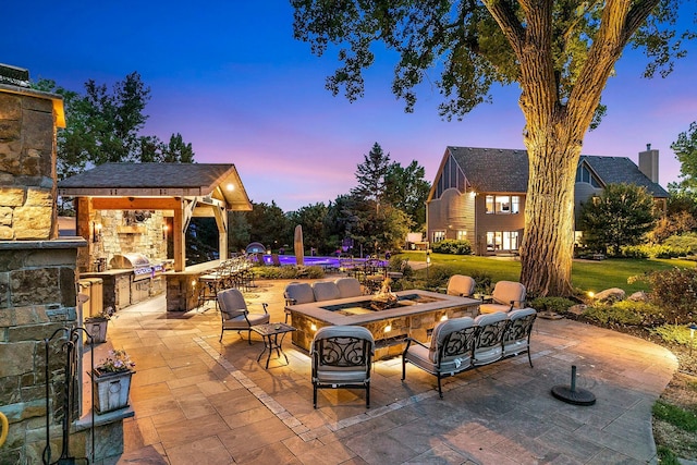 patio terrace at dusk with area for grilling, grilling area, and an outdoor living space with a fire pit