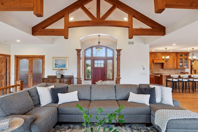 living room featuring beamed ceiling, wood-type flooring, decorative columns, a chandelier, and french doors