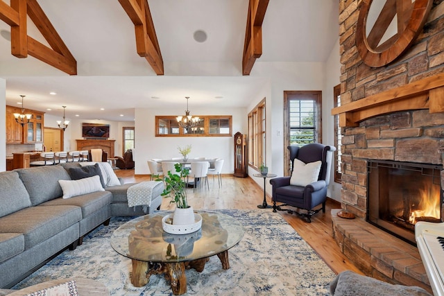 living room with light wood-type flooring, a stone fireplace, lofted ceiling with beams, and a notable chandelier