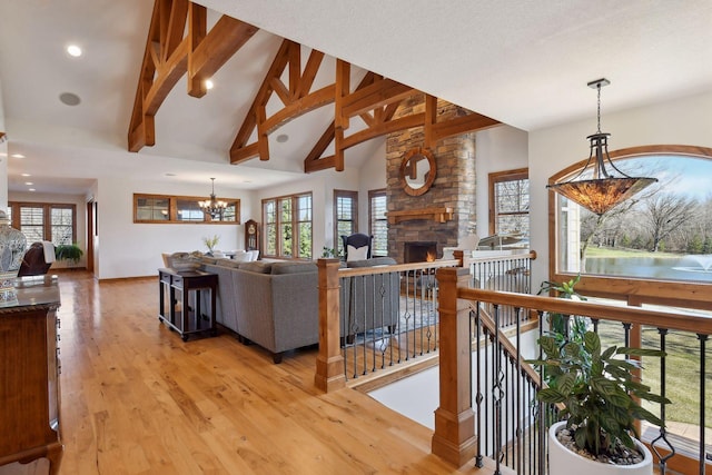 living room featuring an inviting chandelier, a stone fireplace, beam ceiling, and light hardwood / wood-style flooring