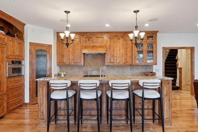 kitchen featuring a kitchen bar, an inviting chandelier, light stone counters, hanging light fixtures, and oven