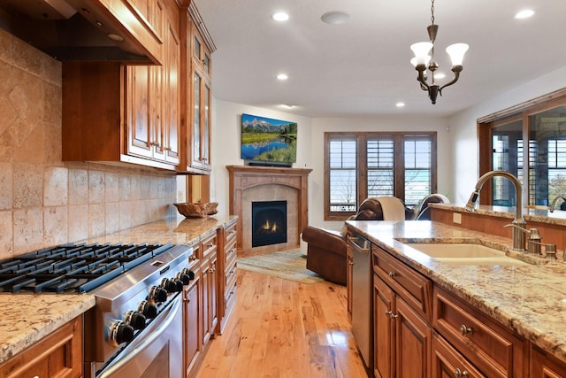 kitchen with sink, light stone counters, ventilation hood, hanging light fixtures, and stainless steel appliances