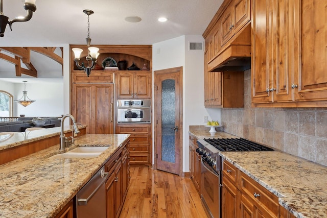 kitchen featuring sink, light hardwood / wood-style flooring, appliances with stainless steel finishes, light stone countertops, and decorative light fixtures