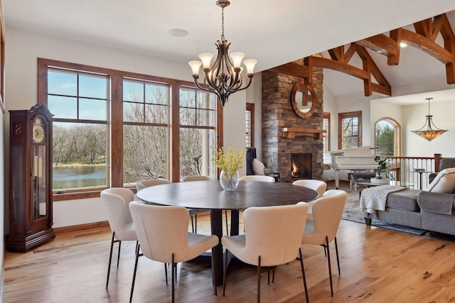 dining room featuring a large fireplace, a notable chandelier, light hardwood / wood-style flooring, and vaulted ceiling with beams