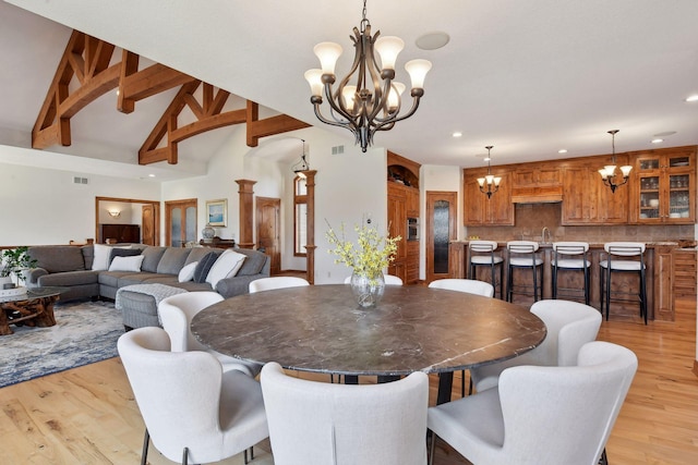 dining room with a notable chandelier, vaulted ceiling with beams, sink, and light wood-type flooring