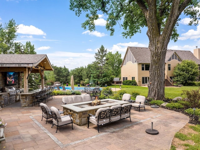 view of patio featuring an outdoor kitchen, grilling area, a pool, exterior bar, and a fire pit