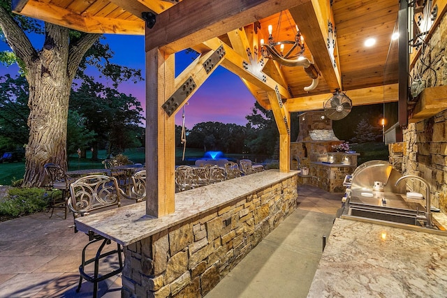 patio terrace at dusk featuring area for grilling, a gazebo, and an outdoor bar