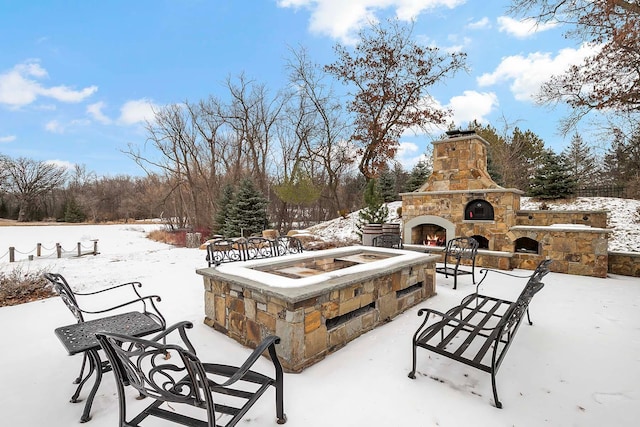 snow covered patio with an outdoor stone fireplace