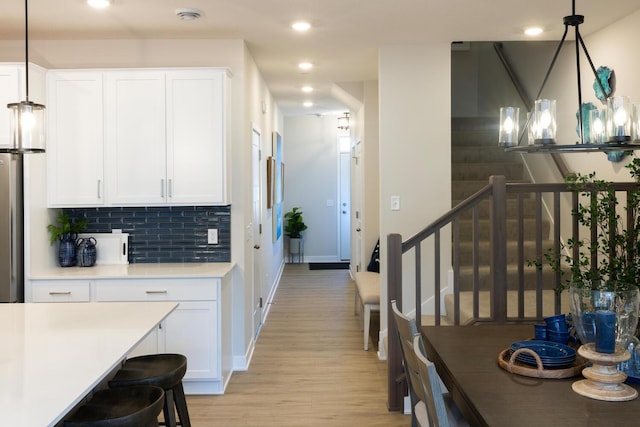 kitchen featuring pendant lighting, an inviting chandelier, tasteful backsplash, light hardwood / wood-style floors, and white cabinets