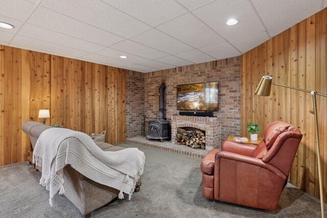 living area featuring a paneled ceiling, a wood stove, wood walls, carpet floors, and recessed lighting