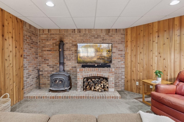 carpeted living area with a drop ceiling, a wood stove, and wood walls