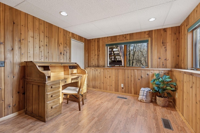 home office featuring baseboards, wooden walls, light wood finished floors, and visible vents