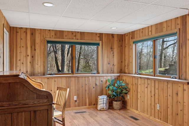 living area with baseboards, wooden walls, visible vents, and wood finished floors