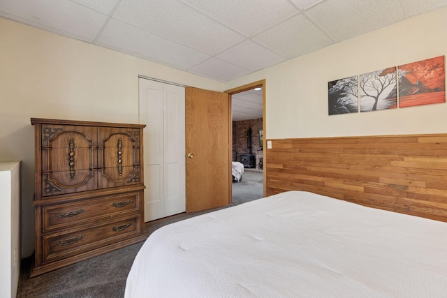 bedroom with a paneled ceiling, wood walls, carpet, and a closet
