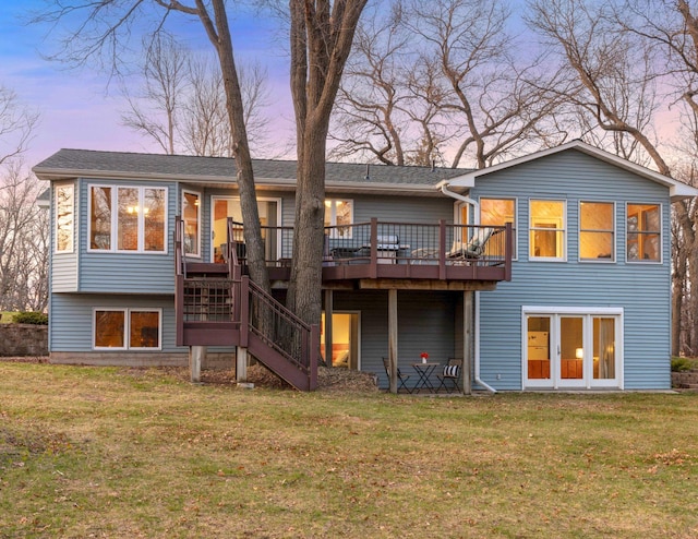 back of house at dusk with a lawn, a deck, and stairs