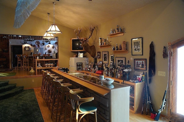 bar featuring lofted ceiling, hardwood / wood-style floors, and white fridge