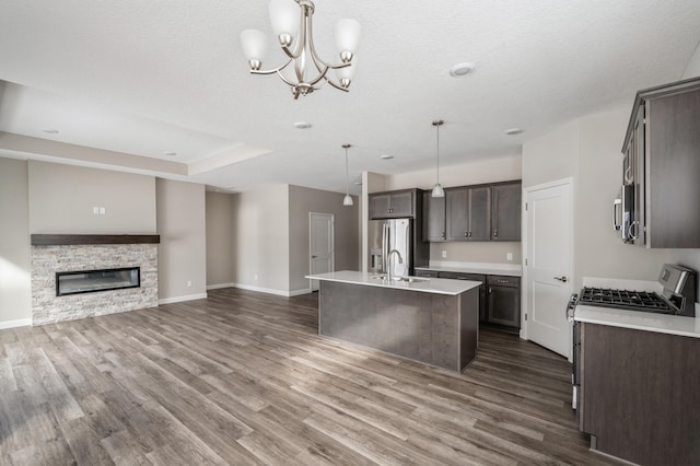 kitchen with pendant lighting, dark brown cabinets, stainless steel appliances, a fireplace, and a center island with sink