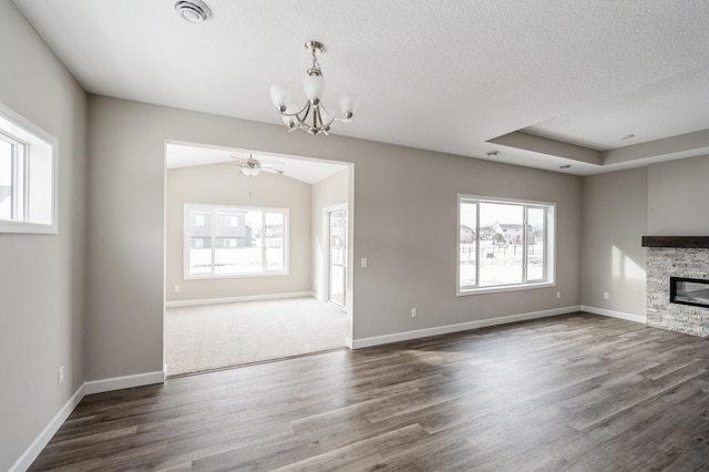 unfurnished living room with dark hardwood / wood-style flooring, ceiling fan with notable chandelier, a fireplace, and a textured ceiling