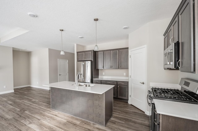 kitchen with appliances with stainless steel finishes, decorative light fixtures, sink, dark hardwood / wood-style flooring, and a center island with sink