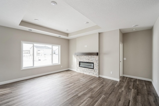 unfurnished living room featuring dark hardwood / wood-style flooring, a tray ceiling, a stone fireplace, and a textured ceiling