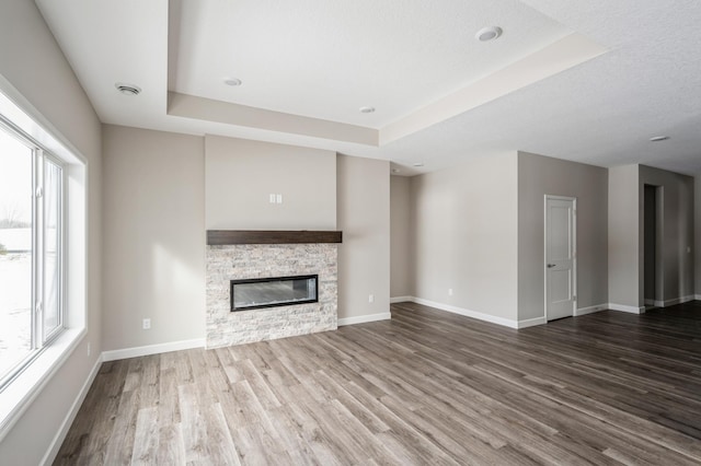 unfurnished living room featuring hardwood / wood-style flooring, a fireplace, a raised ceiling, and a textured ceiling