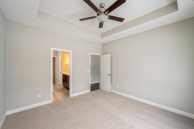 unfurnished bedroom featuring light carpet, a tray ceiling, and ensuite bathroom