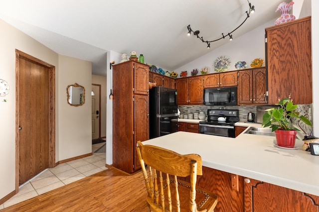 kitchen featuring lofted ceiling, light hardwood / wood-style flooring, kitchen peninsula, decorative backsplash, and black appliances