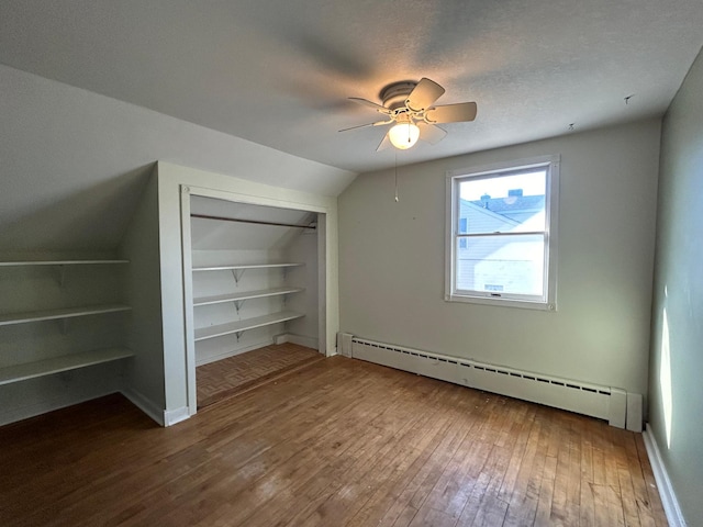 bonus room featuring built in shelves, wood-type flooring, vaulted ceiling, a textured ceiling, and baseboard heating