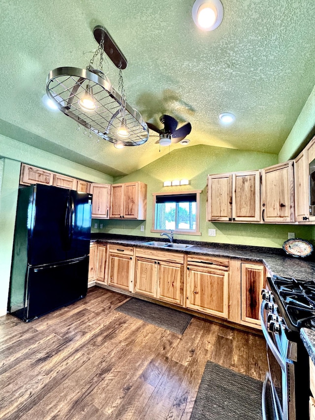 kitchen with vaulted ceiling, black refrigerator, dark hardwood / wood-style floors, sink, and stainless steel gas range oven