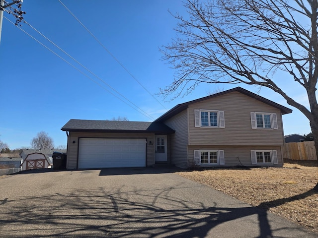 split level home featuring a garage, aphalt driveway, and fence