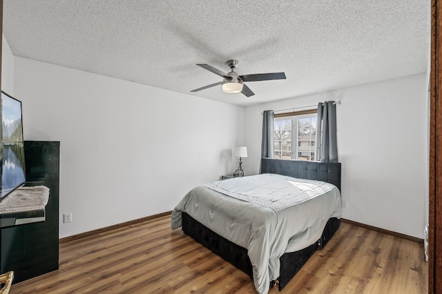 bedroom with ceiling fan, a textured ceiling, baseboards, and wood finished floors