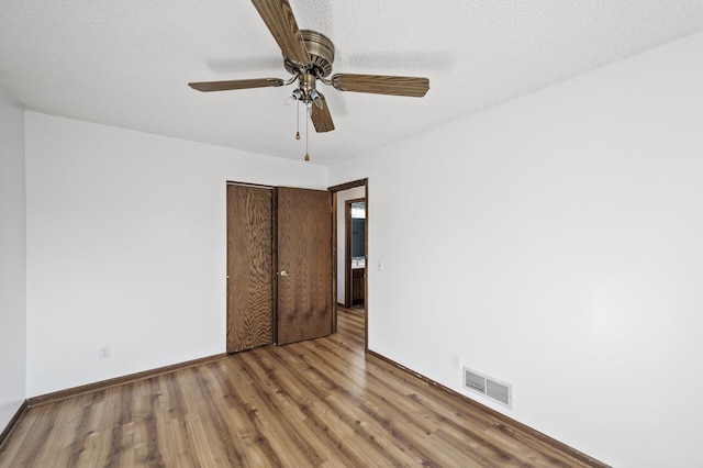 unfurnished bedroom featuring visible vents, a ceiling fan, a textured ceiling, wood finished floors, and a closet