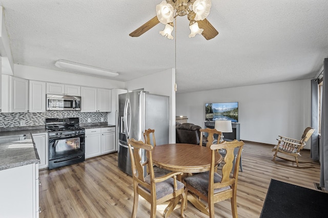 dining space with light wood-style flooring, a ceiling fan, baseboards, and a textured ceiling