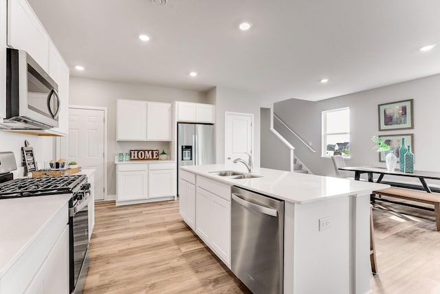 kitchen with sink, light hardwood / wood-style flooring, appliances with stainless steel finishes, white cabinetry, and a center island with sink