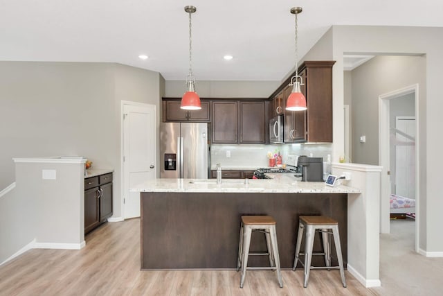 kitchen featuring sink, stainless steel appliances, tasteful backsplash, dark brown cabinetry, and light stone countertops