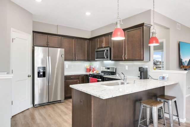 kitchen with sink, dark brown cabinets, hanging light fixtures, appliances with stainless steel finishes, and light stone countertops