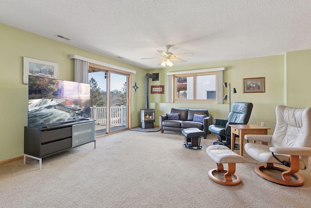 carpeted living room with ceiling fan, a wood stove, and a textured ceiling