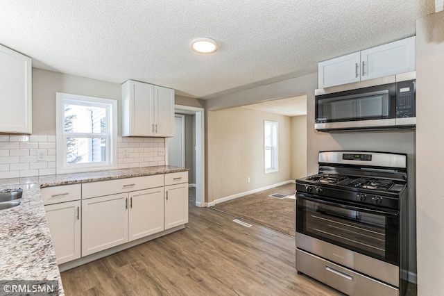 kitchen with white cabinetry, stainless steel appliances, light stone countertops, and light hardwood / wood-style flooring