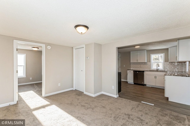 kitchen featuring sink, dishwasher, white cabinetry, backsplash, and carpet