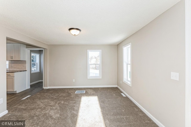 unfurnished dining area featuring dark carpet, a wealth of natural light, and a textured ceiling