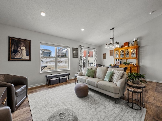 living room featuring lofted ceiling, a notable chandelier, light hardwood / wood-style flooring, and a textured ceiling