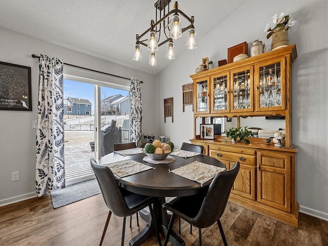 dining area with dark hardwood / wood-style flooring, a notable chandelier, vaulted ceiling, and a textured ceiling