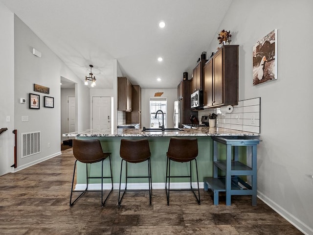 kitchen featuring sink, backsplash, dark hardwood / wood-style floors, a kitchen bar, and kitchen peninsula