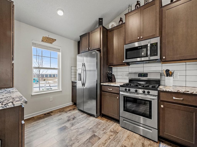 kitchen with stainless steel appliances, backsplash, dark brown cabinetry, and light hardwood / wood-style floors