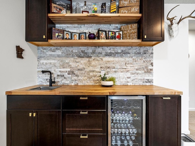 bar featuring butcher block counters, sink, dark brown cabinets, beverage cooler, and backsplash