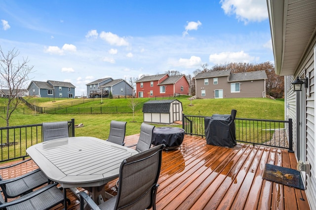 wooden terrace with a residential view, a storage unit, a yard, an outdoor structure, and outdoor dining space