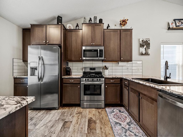 kitchen featuring lofted ceiling, light wood-style flooring, a sink, appliances with stainless steel finishes, and decorative backsplash