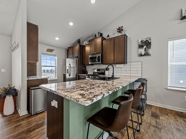 kitchen with stainless steel appliances, a sink, a kitchen breakfast bar, backsplash, and dark wood finished floors